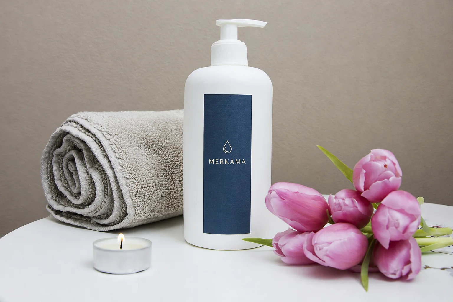 A considered Merkama product arrangement with a branded pump bottle, towel, and candle